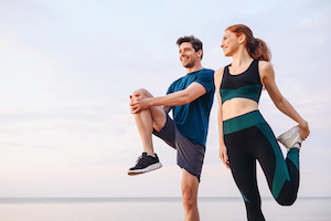 En sporty kvinne og mann i sportsklær som varmer opp med stretching før en joggerunde